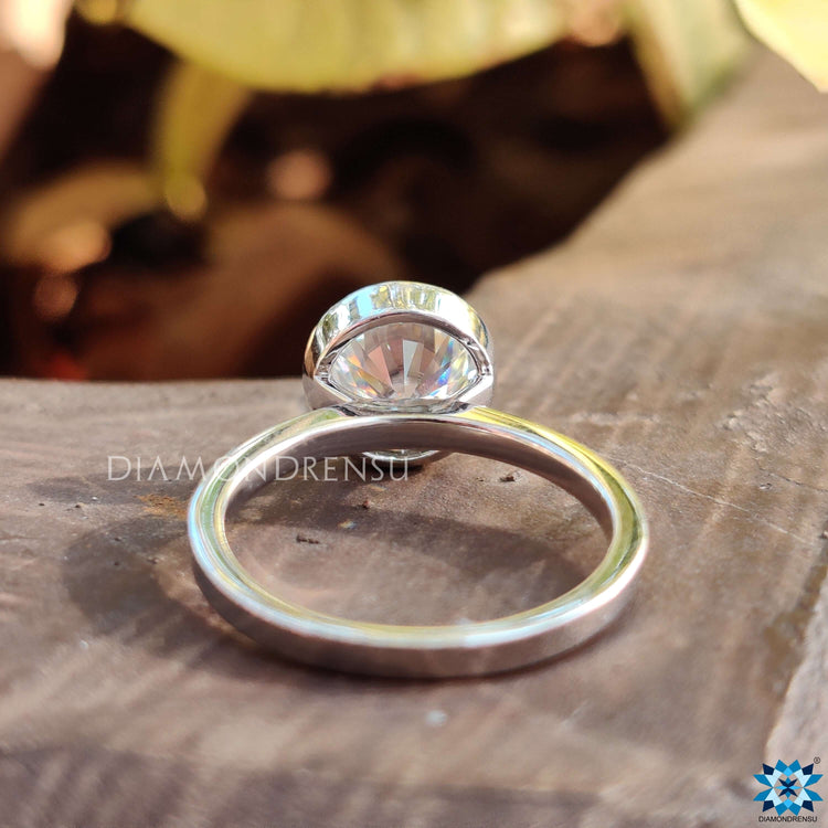 Diamondrensu UK ring featuring white gold band and round bezel Moissanite.
