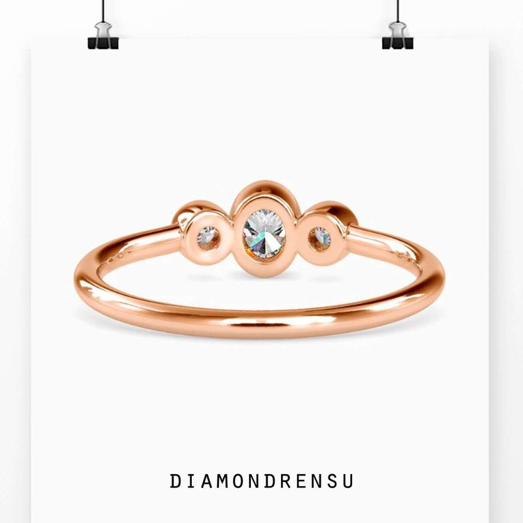 Oval diamond engagement ring with bezel set round stones in rose gold.
