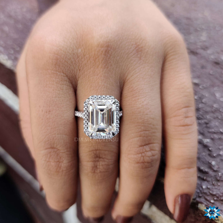 White gold ring featuring emerald cut center and round halo.

