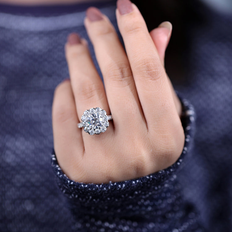 Cushion moissanite ring with halo setting and round cut pave band.
