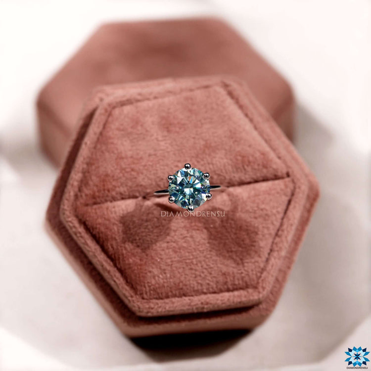 Custom round engagement ring with a cyan blue moissanite and prong setting.
