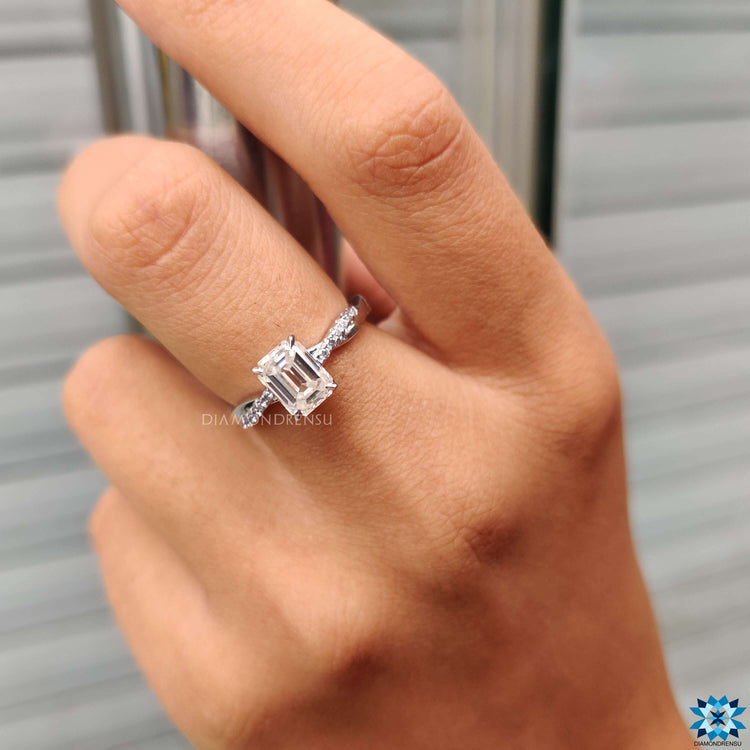 White gold engagement ring with emerald and round cut stones.
