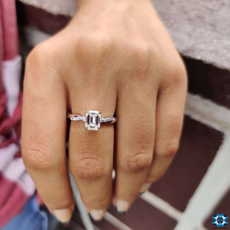 Elegant moissanite ring with emerald center and round accents.
