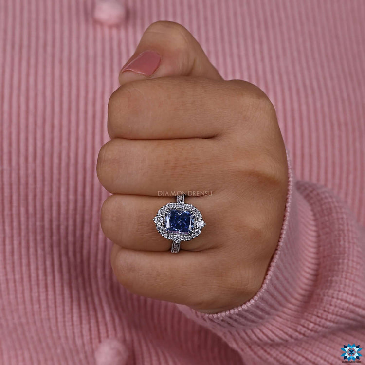Moissanite halo ring featuring blue radiant cut center stone.
