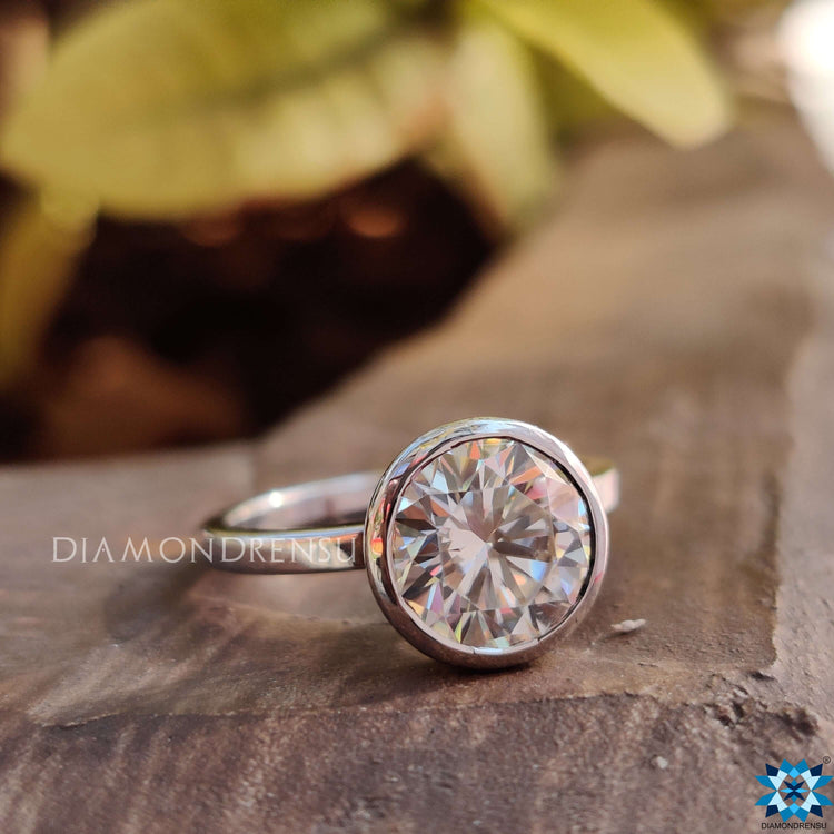 Custom engagement ring with round bezel-set Moissanite in sleek white gold.
