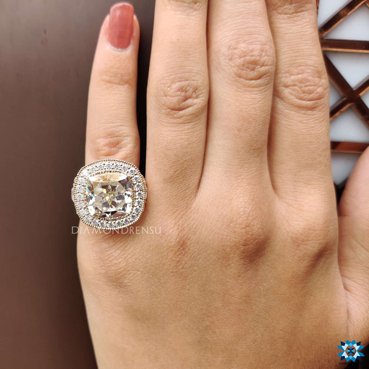 Yellow gold cushion cut moissanite ring with milgrain detailing.
