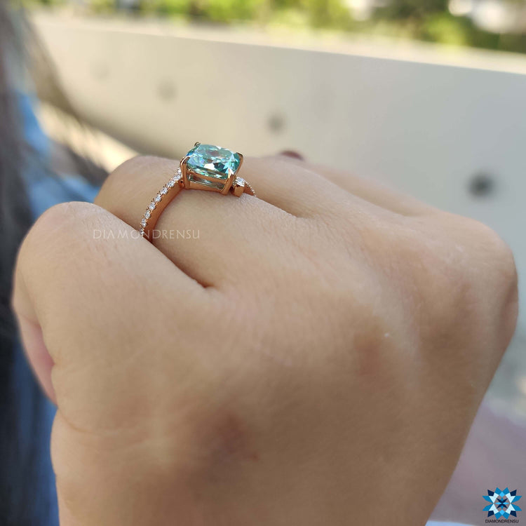 Blue moissanite ring with compass prongs and side stone accents.
