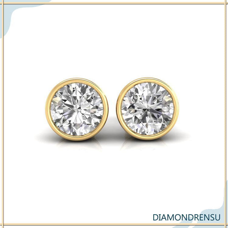 UK diamond earrings featuring bezel set round diamonds in gold studs.
