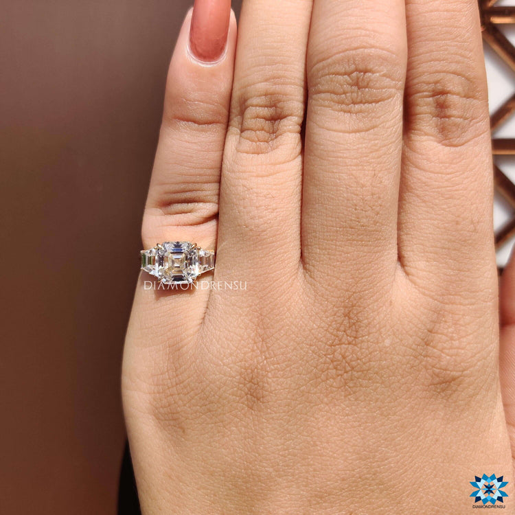 Three stone engagement ring featuring asscher cut center and claw prong setting.
