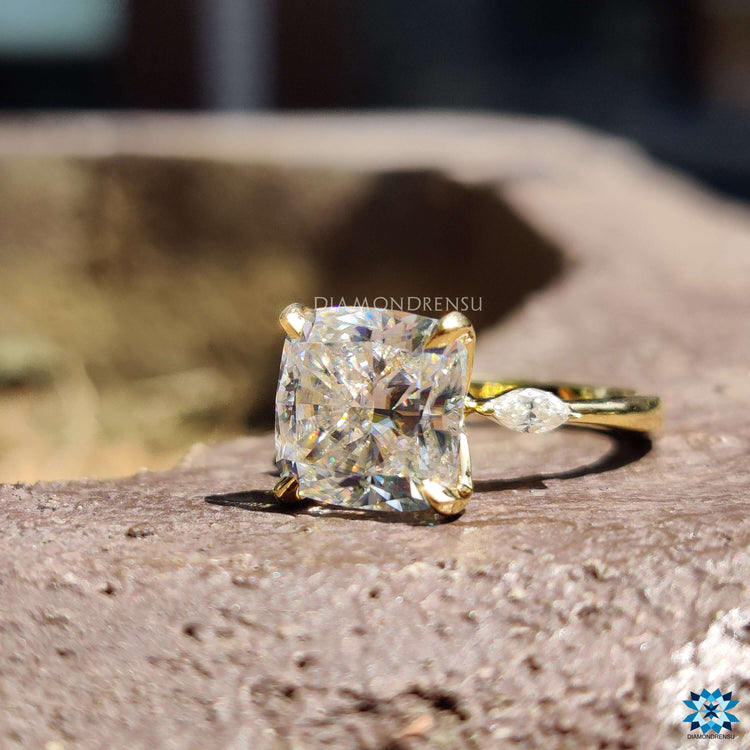 Yellow gold ring featuring a cushion moissanite and pear side stones.

