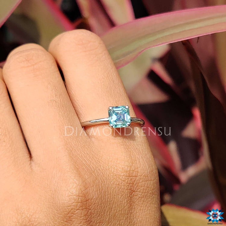 Four prong setting ring holding a cyan blue moissanite stone.

