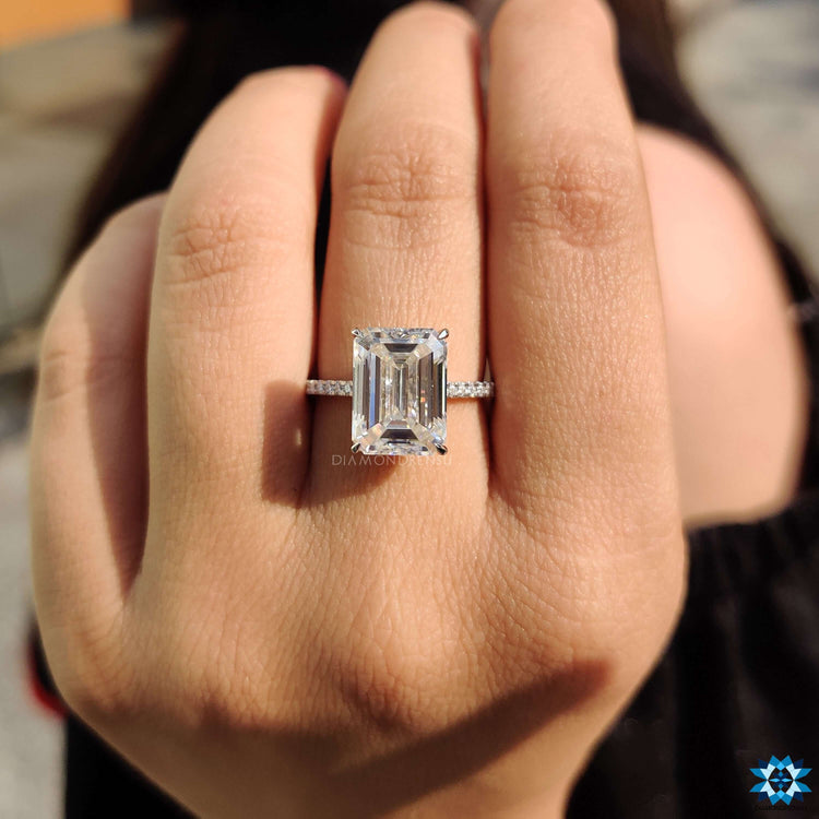 White gold ring featuring emerald cut center stone and pave band.
