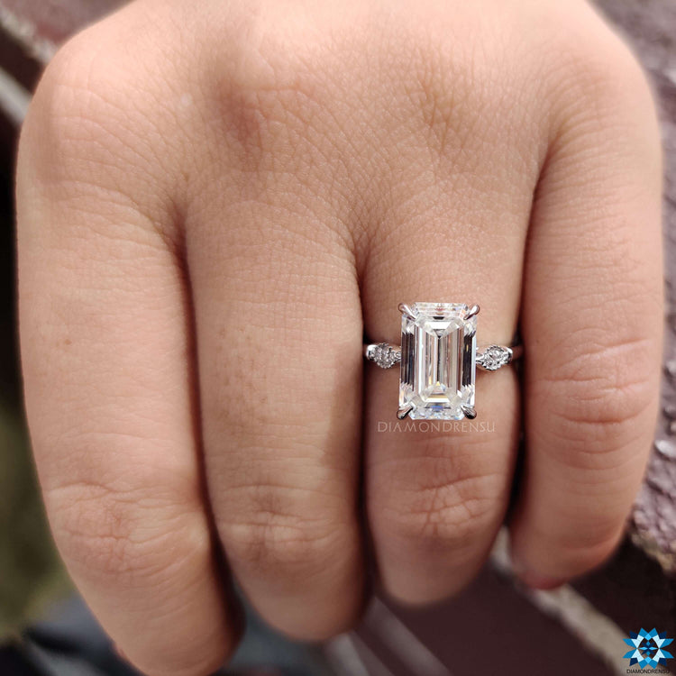 Engagement ring with emerald cut center and round side stones.
