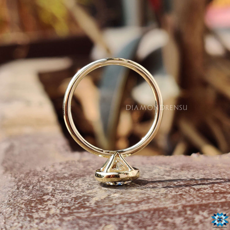 Yellow gold engagement ring with round moissanite in bezel mount.
