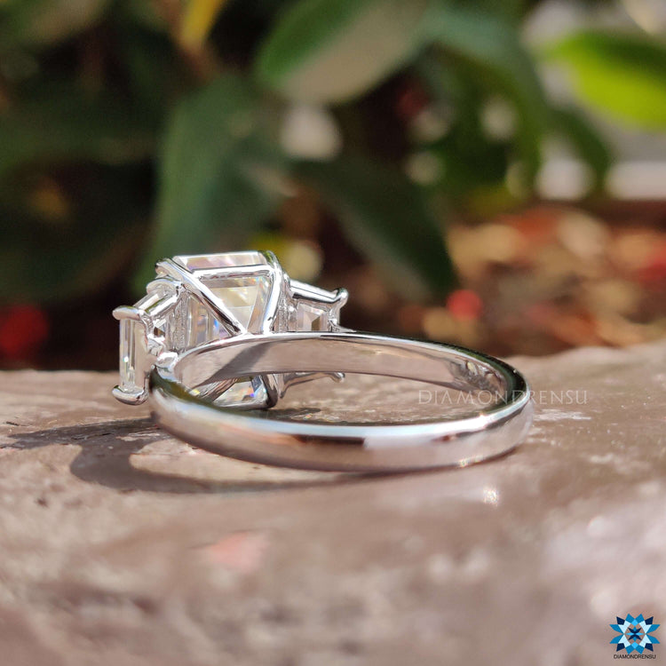 White gold moissanite ring with emerald and trapezoid cut stones.
