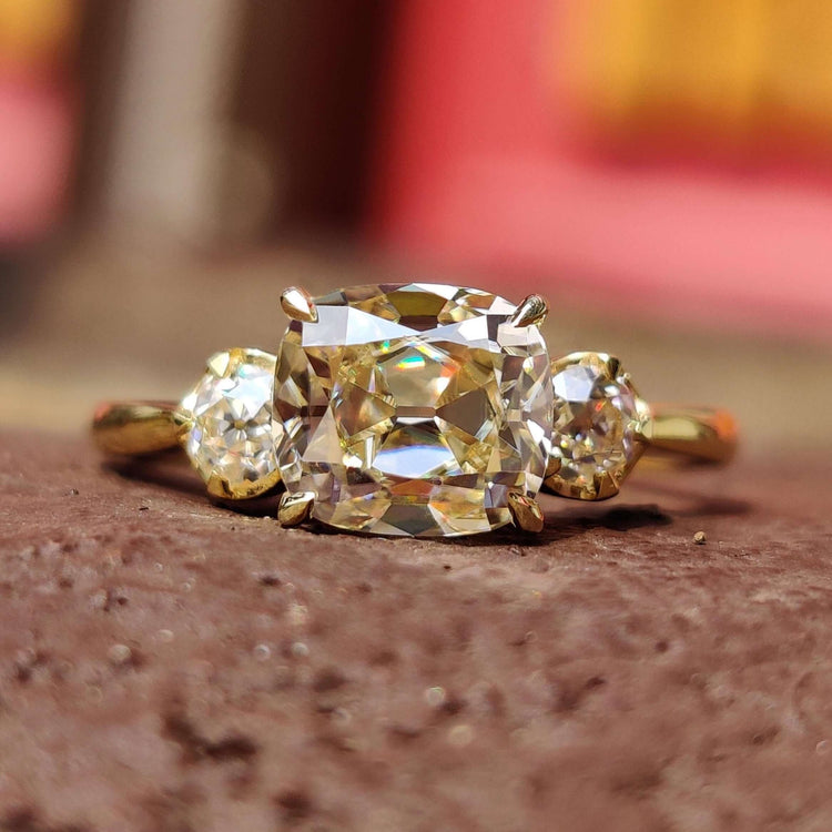 3 stone engagement ring featuring a cushion old mine cut center stone and round old European side stones.
