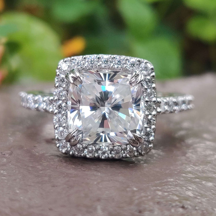 Cushion cut moissanite ring with halo and pavé band.
