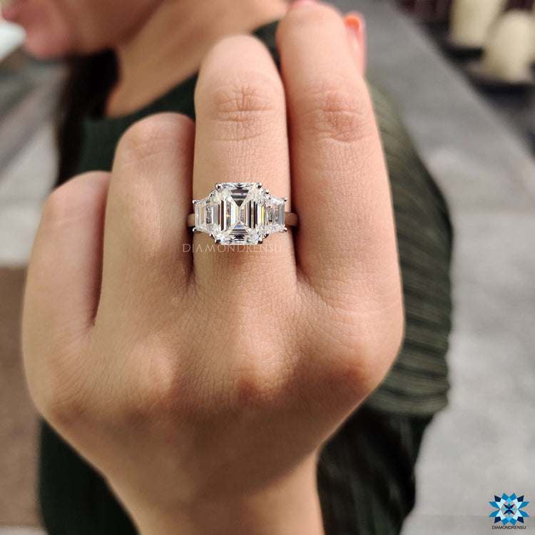Emerald centre stone ring with trapezoid accents in a cathedral setting.
