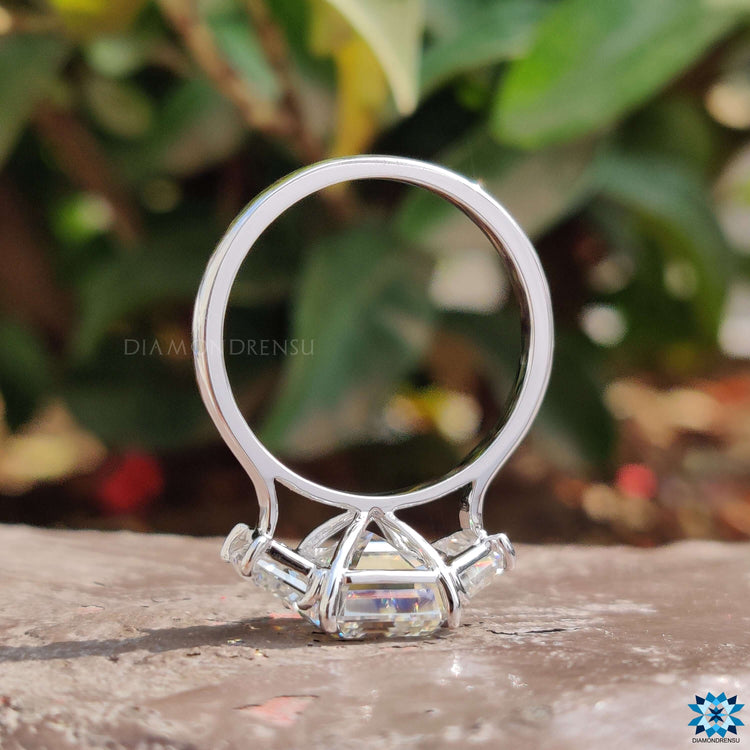 Prong setting ring showcasing emerald moissanite and trapezoid side stones.
