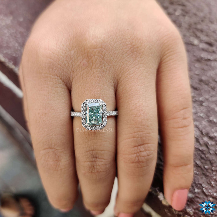 Light cyan blue radiant engagement ring with round cut side stones and hidden halo.
