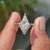 White gold engagement ring featuring kite cut moissanite and half halo.
