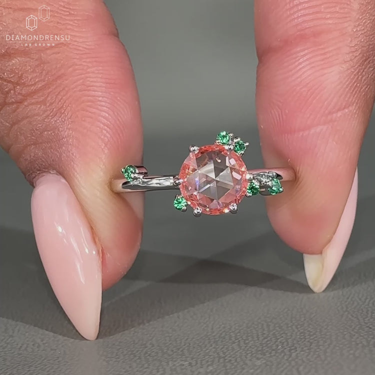 Peach sapphire ring with green emerald side stones cluster.