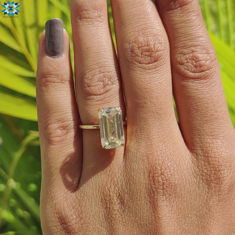Solitaire ring featuring emerald cut moissanite in a classic gold band.
