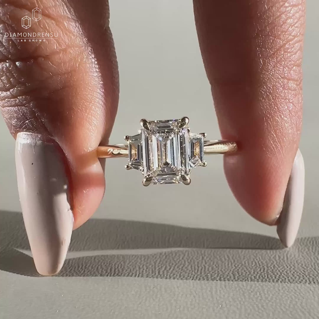 Close-up of a lab grown diamond ring with emerald cut center and trapezoid side diamonds, held in single claw prongs