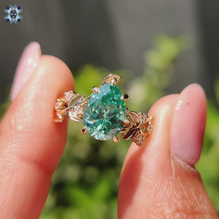 Nature inspired engagement ring featuring a pear shaped green moissanite center stone.
