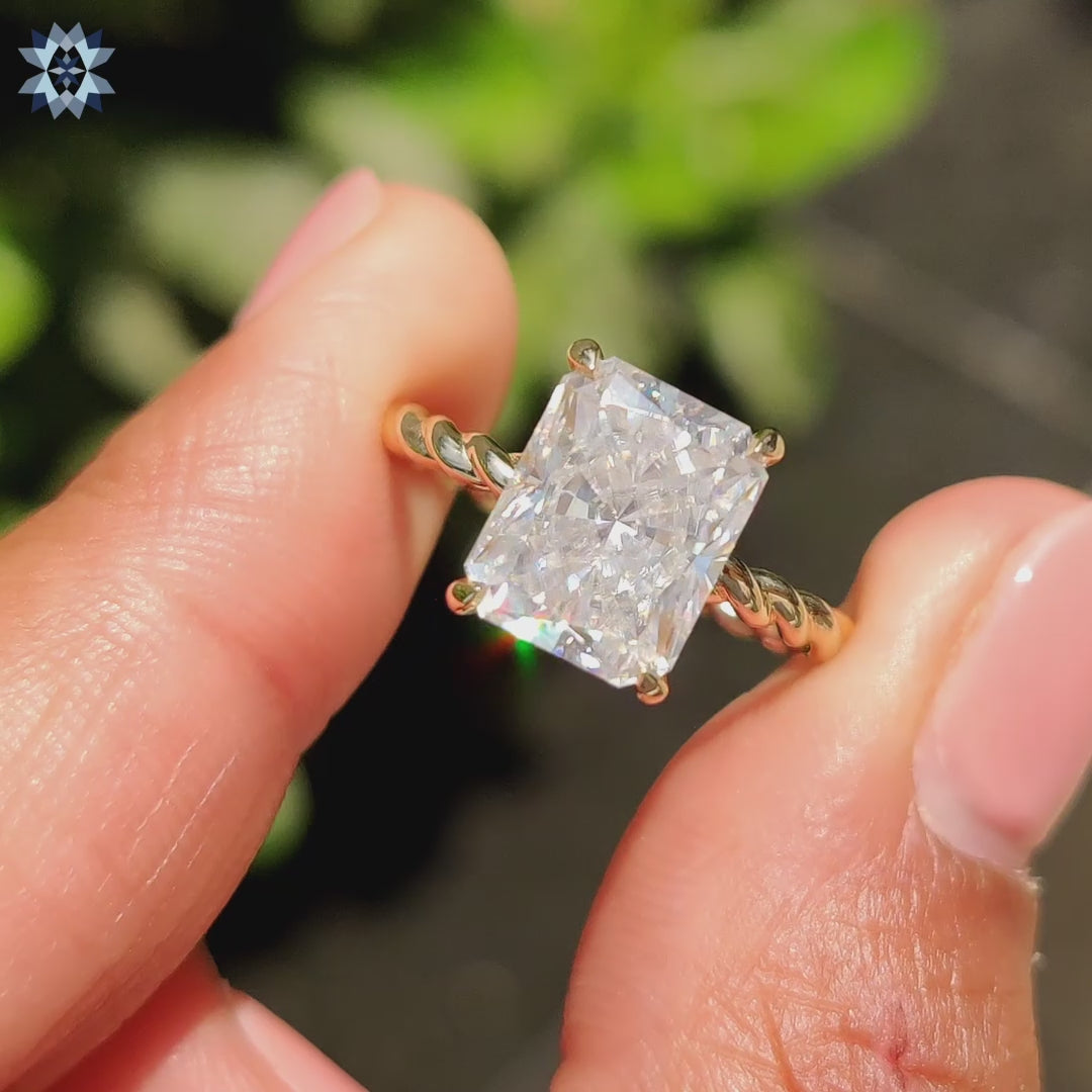 Twisted band yellow gold ring featuring radiant cut moissanite centre.
