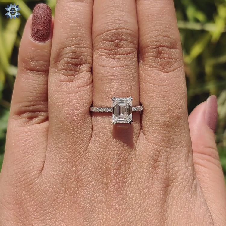 Prong set emerald cut moissanite ring designed with a pave band.
