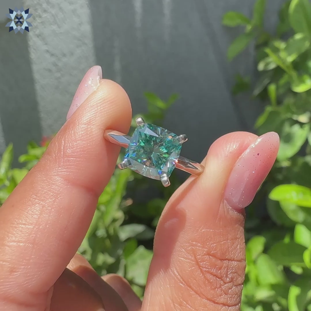Cyan blue cushion cut moissanite ring with four tab prong setting and hammer finish.
