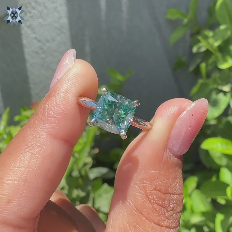 Cyan blue cushion cut moissanite ring with four tab prong setting and hammer finish.
