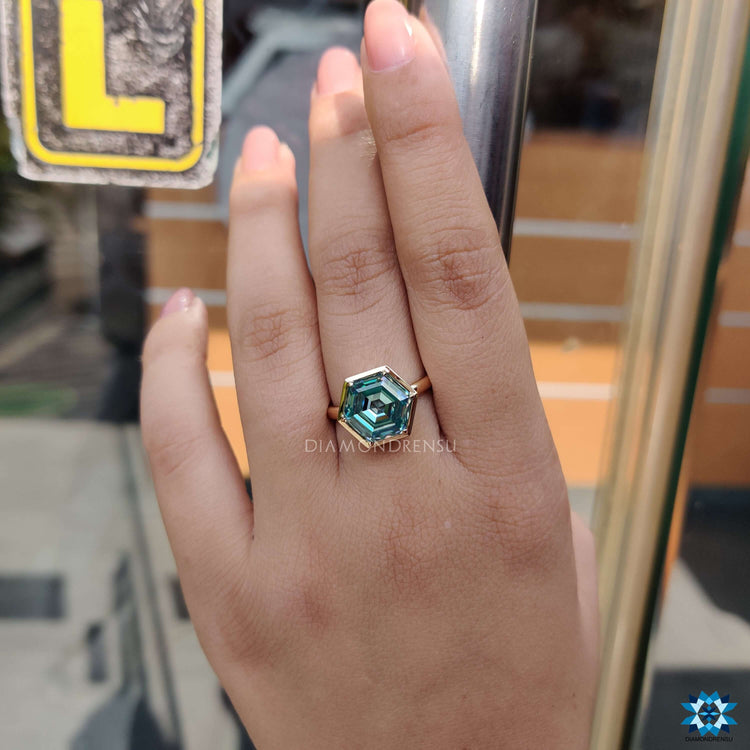 Solitaire moissanite engagement ring with yellow gold bezel setting.
