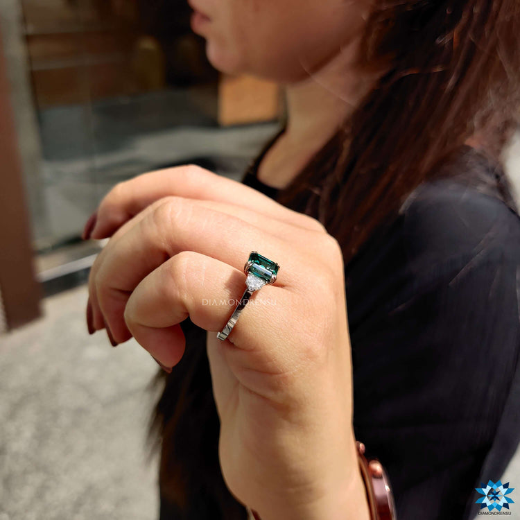 White gold ring with Asscher cut center and two side halos.
