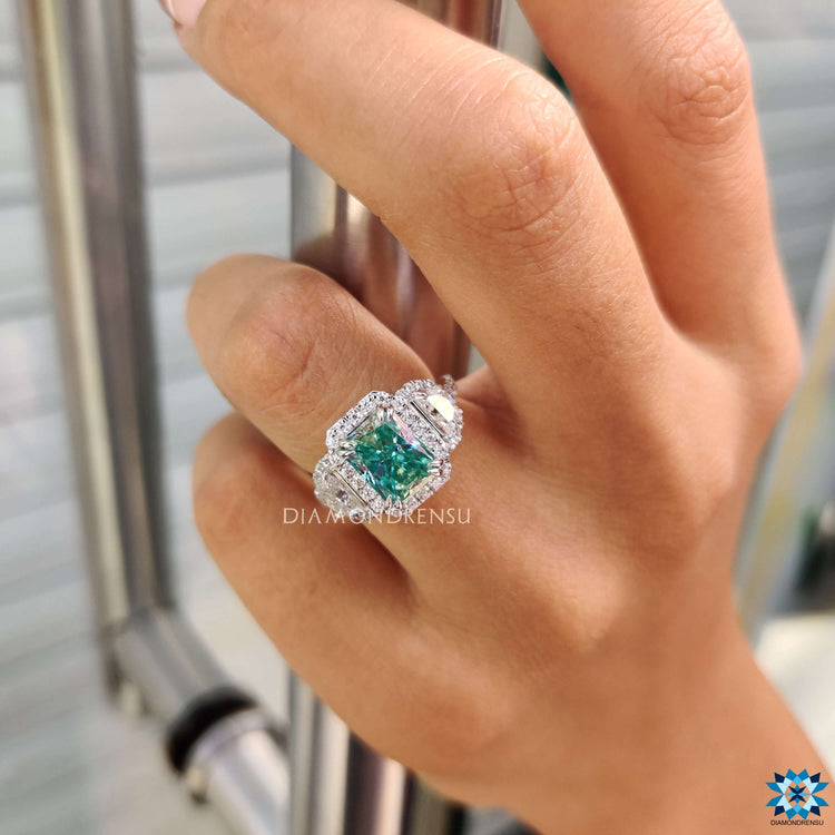 Radiant cut cyan moissanite ring with round pave accents.
