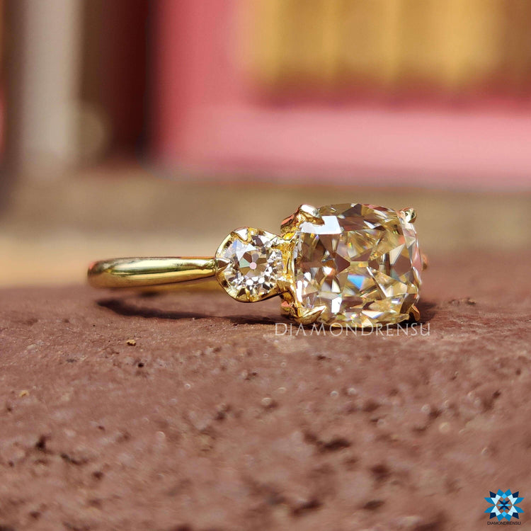 Light yellow moissanite ring with a cushion old mine cut center and matching side stones.
