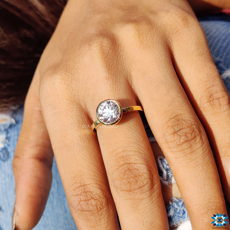 Bezel solitaire ring with round cut Moissanite in handcrafted yellow gold.
