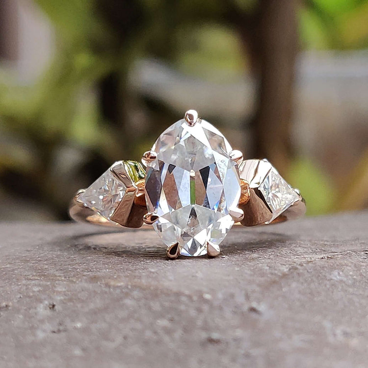 Three stone moissanite ring in rose gold with claw prongs.
