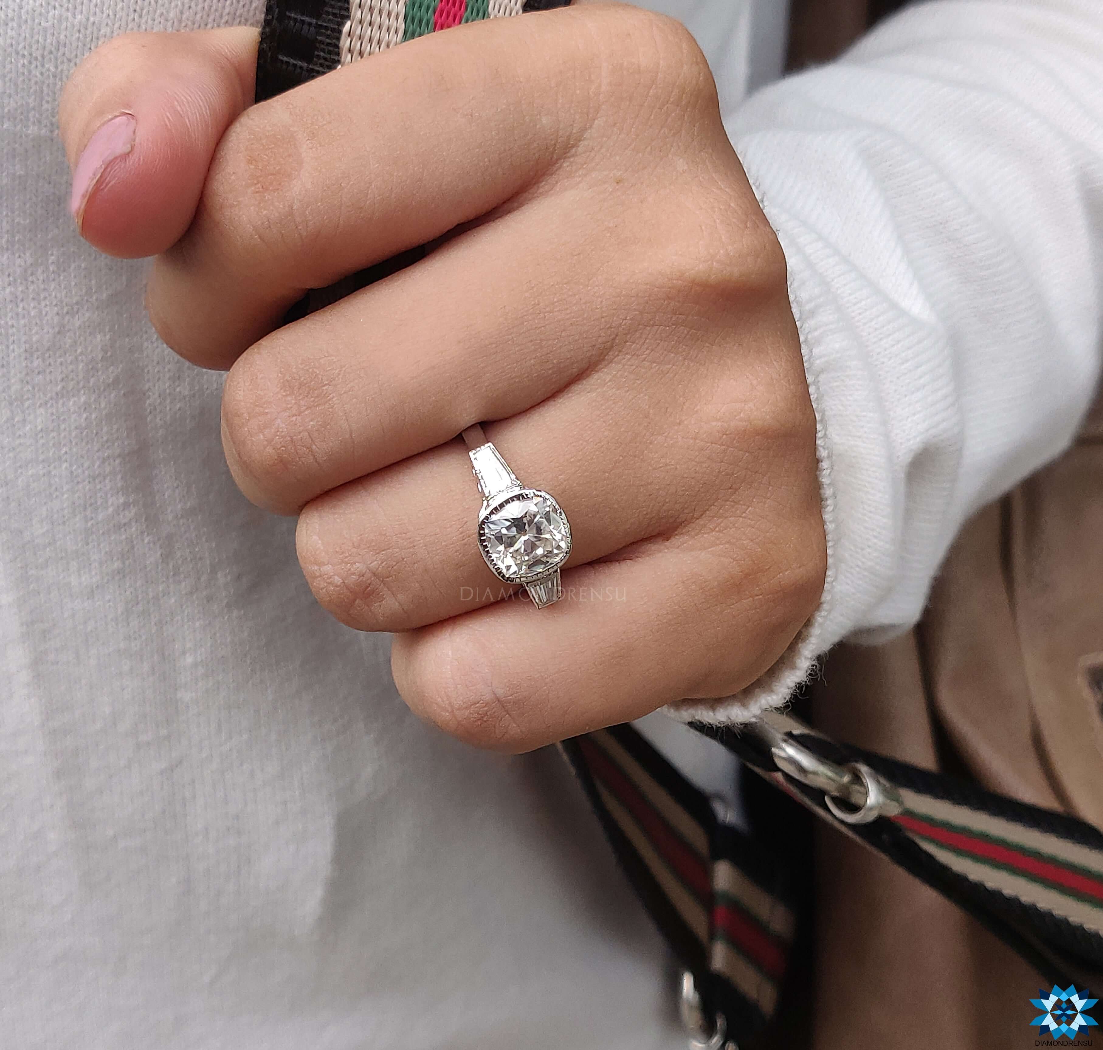 Bezel setting ring featuring a cushion-cut moissanite centre and tapered baguette stones.