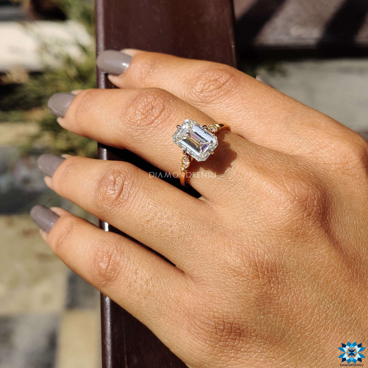 Buy emerald cut moissanite ring with round cut side stones.
