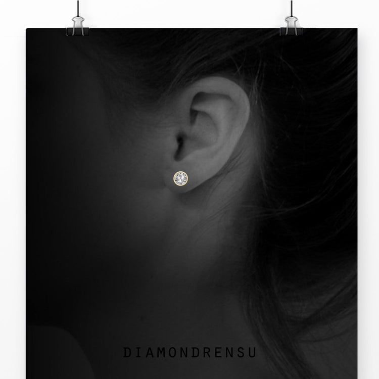 Handmade gold stud earrings featuring round bezel set diamonds.
